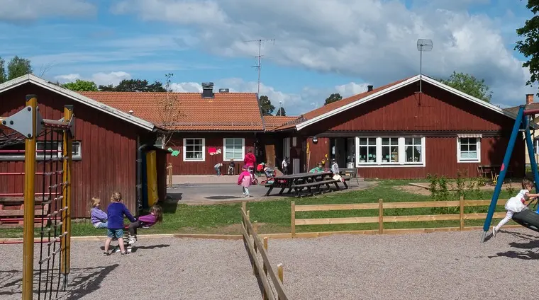 Förskolan Rosen och gården med klätterställning och gungor samt lekande barn.