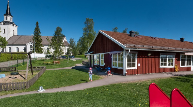 Förskolan Siljansnäs,  som är belägen vid kyrkan. Förskolans utegård med gungställning och rutschkana samt lekande barn syns.
