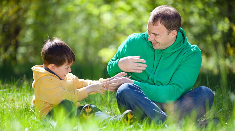 En glad pappa leker med sitt barn i gräset